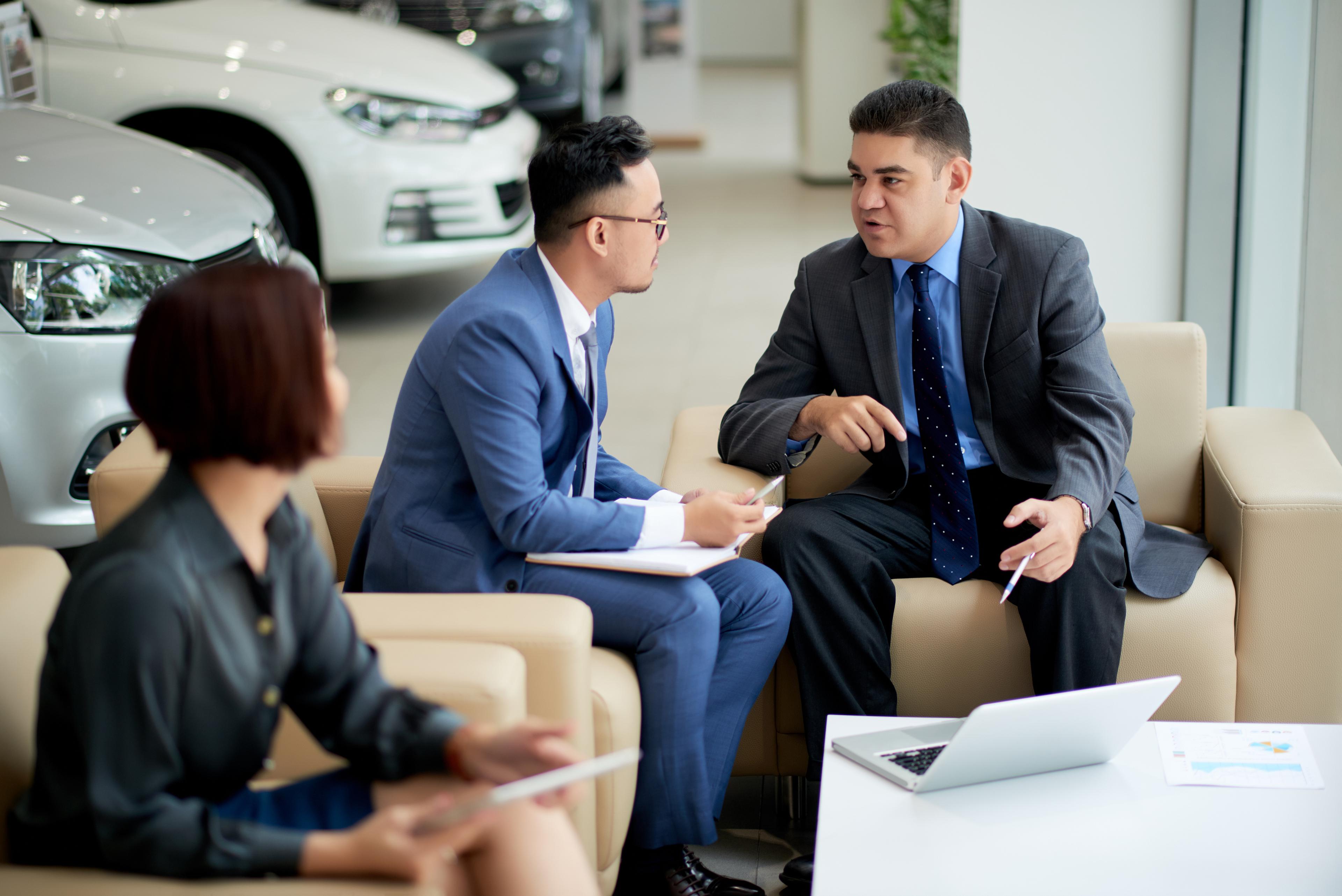 Business customers and sales staff reviewing a new vehicle purchase at a dealership